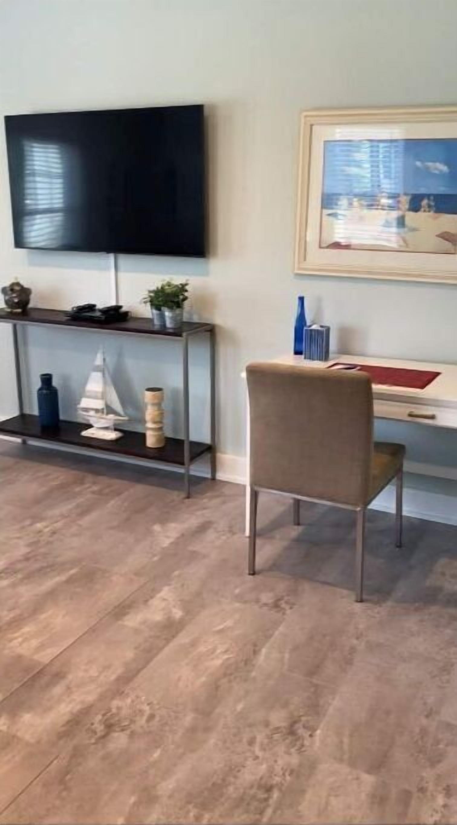 Un salon avec un téléviseur à écran plat fixé au mur, une table basse en bois, un fauteuil beige et un bureau avec un ordinateur.