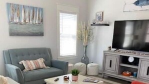 A living room with a grey sofa, a red armchair, a coffee table, and a TV on a wooden stand.