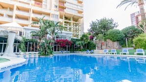 Una piscina con sillas de descanso, rodeada de vegetación y un edificio de varios pisos con balcones.