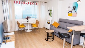 Una sala moderna con un sofá gris, sillas amarillas, una mesa redonda de madera y un taburete.