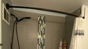 A shower area with a bathtub, a showerhead, and a tiled wall.