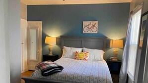 A bedroom with a bed, two bedside tables with lamps, a door, and a wall with a bicycle artwork.