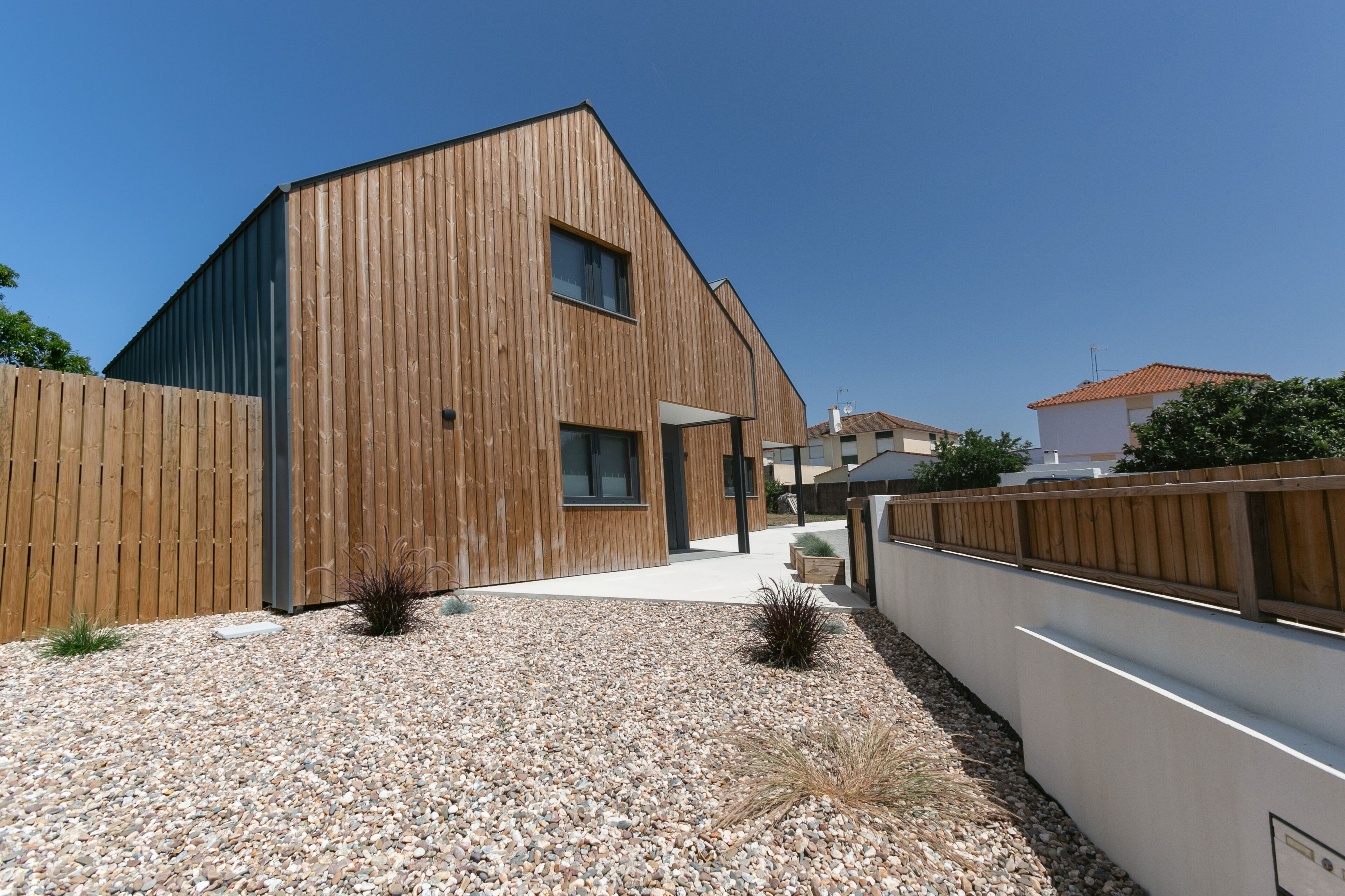Un bâtiment moderne avec une façade en bois, une allée gravillonnée et une clôture en bois.