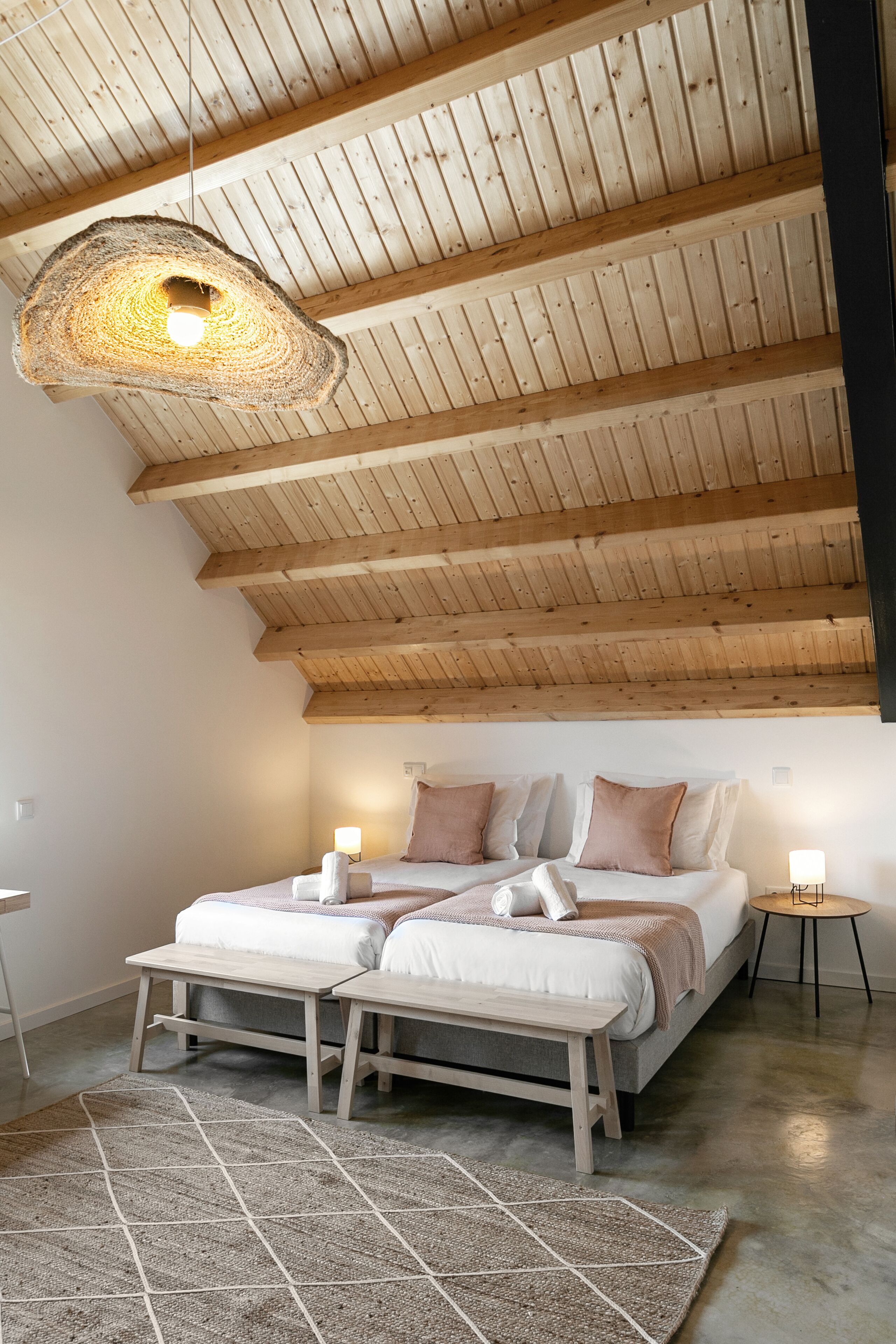 Une chambre avec un plafond en bois incliné, un lit avec deux oreillers, une table de chevet, un luminaire suspendu et un tapis.