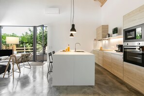 Une cuisine moderne dotée d’un îlot central, d’appareils électroménagers en acier inoxydable et d’une grande fenêtre donnant sur un paysage verdoyant.