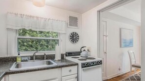 A kitchen with white cabinets, a stove, a sink, and a window with a view of greenery. - #3 Bright 1-Bdrm suite downtown with parking (Saugatuck)