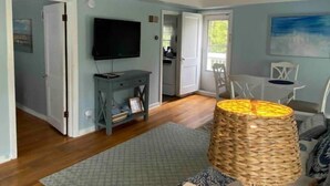 A room with a television, a small table, a wicker lamp, and a door leading to another room. - #3 Bright 1-Bdrm suite downtown with parking (Saugatuck)