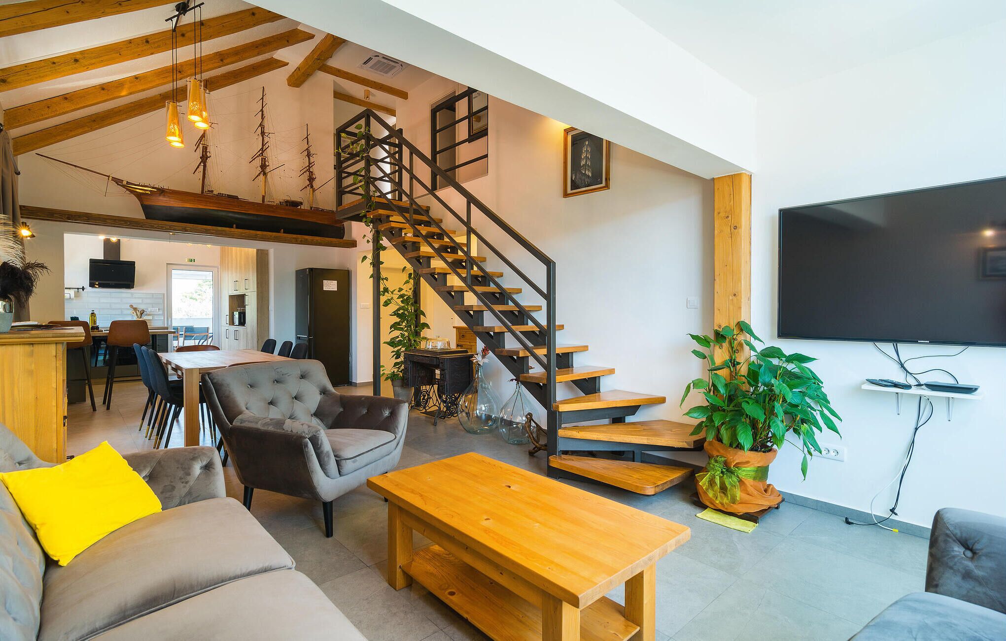 A spacious living area with a wooden staircase, a sofa, a coffee table, and a TV mounted on the wall.