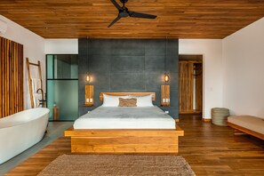 Quarto moderno com teto de madeira, uma cama grande com estrutura de madeira, duas luminárias fixadas na parede e uma banheira branca.