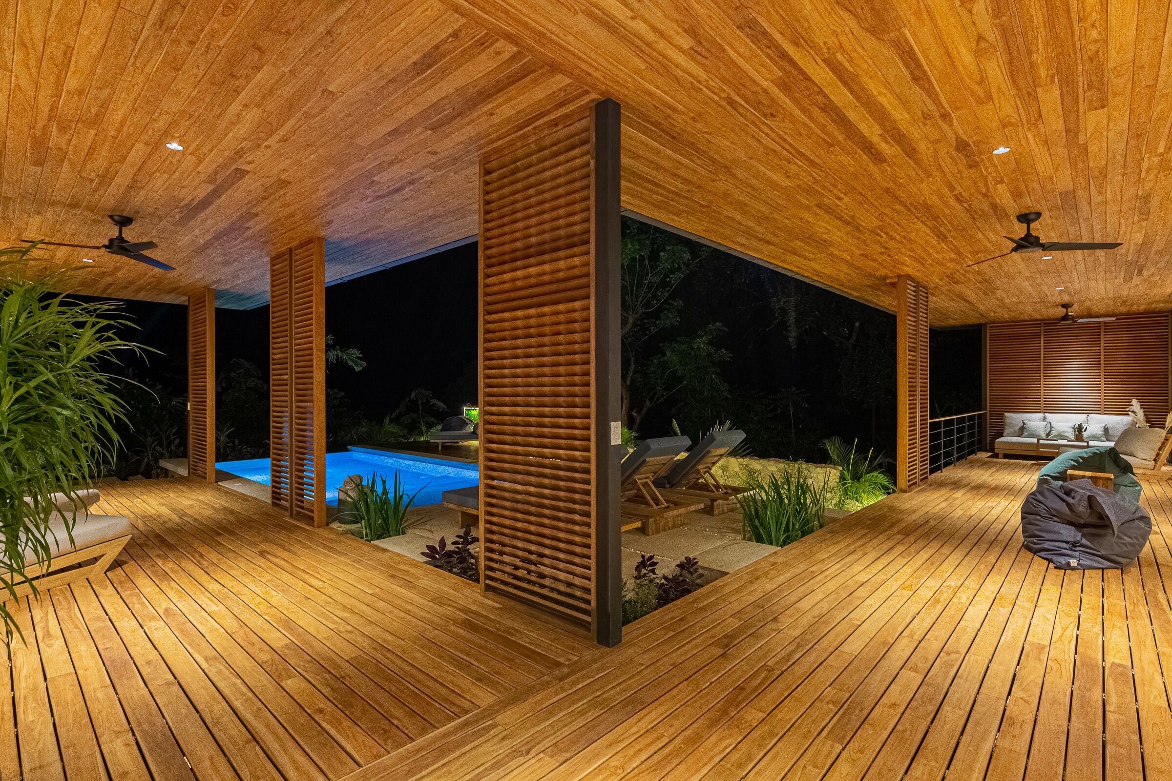 A wooden deck with a pool, lounge chairs, and a sofa.