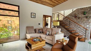 Ein geräumiges Wohnzimmer mit hohen Decken, Holzboden, einem großen Fenster, einer Treppe mit Steinwand und einer modernen Sofagarnitur.
