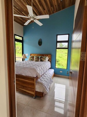 Un dormitorio con cama, ventilador de techo y ventanas amplias.