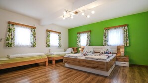 A room with a large bed, two smaller beds, a wooden floor, and green walls. - Ferienhaus mit Landblick (Oberhaag)