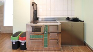 A compact kitchenette with a built-in stove, a sink, and a small oven. There are two trash bins and a window providing natural light. - Ferienhaus mit Landblick (Oberhaag)