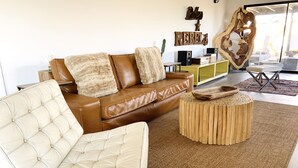 A modern living room with a brown leather sofa, a white tufted armchair, and a wooden coffee table. - Stardust on the Mesa...A Breathtaking Experience (Yucca Valley)