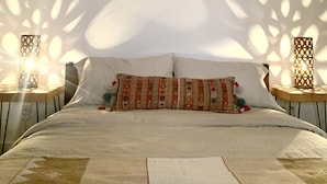 A bed with patterned pillows, two nightstands with lamps, and a decorative ceiling light fixture. - Stardust on the Mesa...A Breathtaking Experience (Yucca Valley)