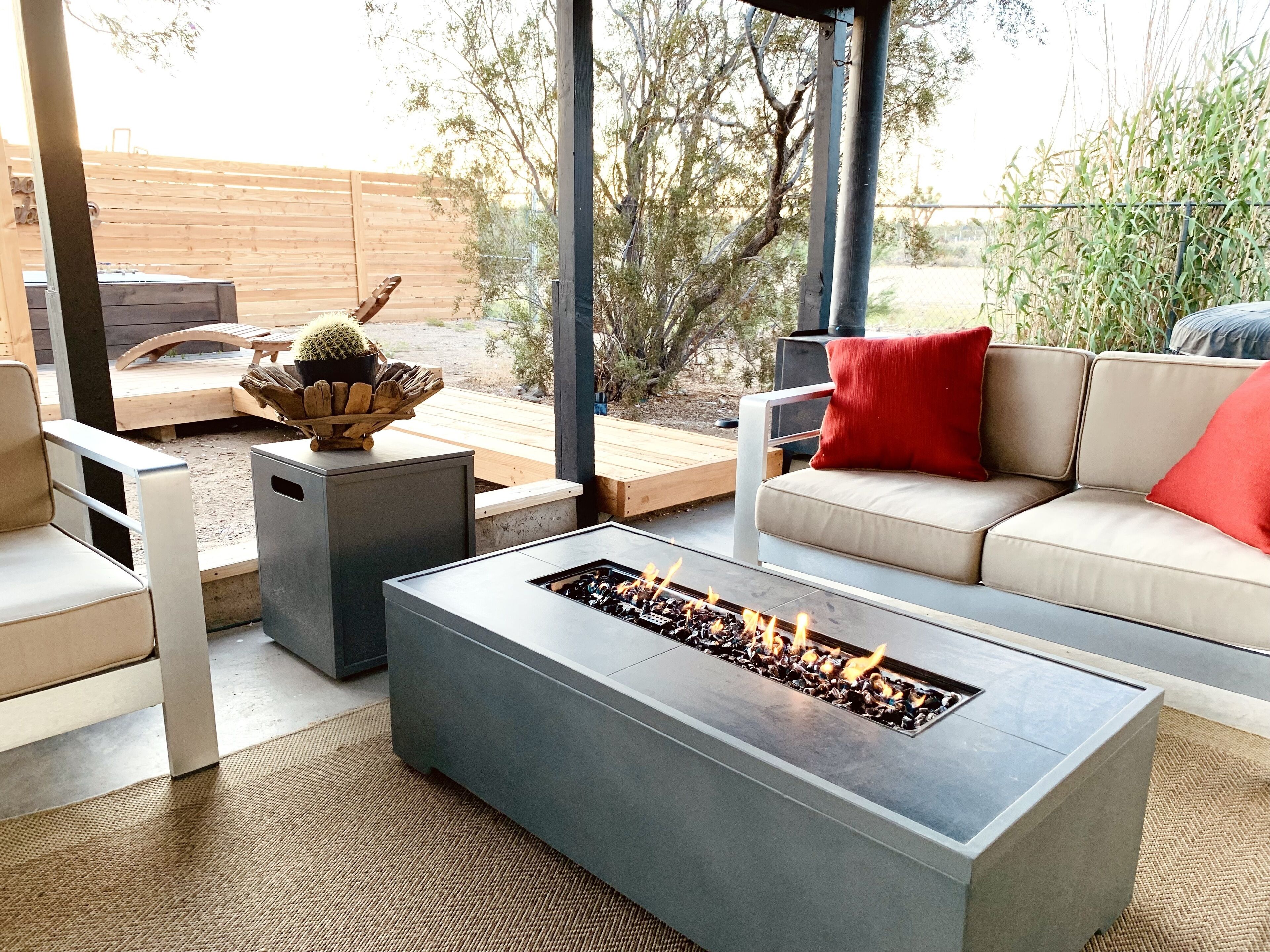 Un área de estar moderna al aire libre con un brasero, un sofá acolchado y una mesa de madera con un cactus como centro.