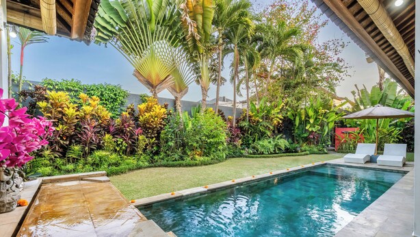 Piscina con jardín circundante, una pequeña cascada y una zona de estar cubierta.