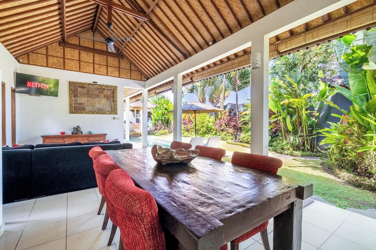 A spacious indoor area with a wooden ceiling, a dining table with red chairs, a sofa, and a wall-mounted Netflix sign.