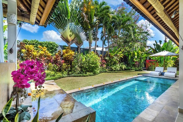 A swimming pool with a tiled edge, surrounded by lush greenery and palm trees. - Romantica Villa (Ubud)