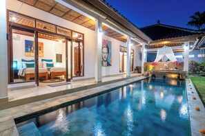 A poolside area with a clear view of a bedroom with two beds, a large painting, and a decorative wall. - Romantica Villa (Ubud)