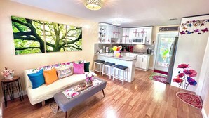 A modern kitchen with white cabinets, a central island with bar stools, and a large window with a tree view. - Boutique Guest House – Private Patio Oasis – Near Beach – Family-Friendly (North Miami)