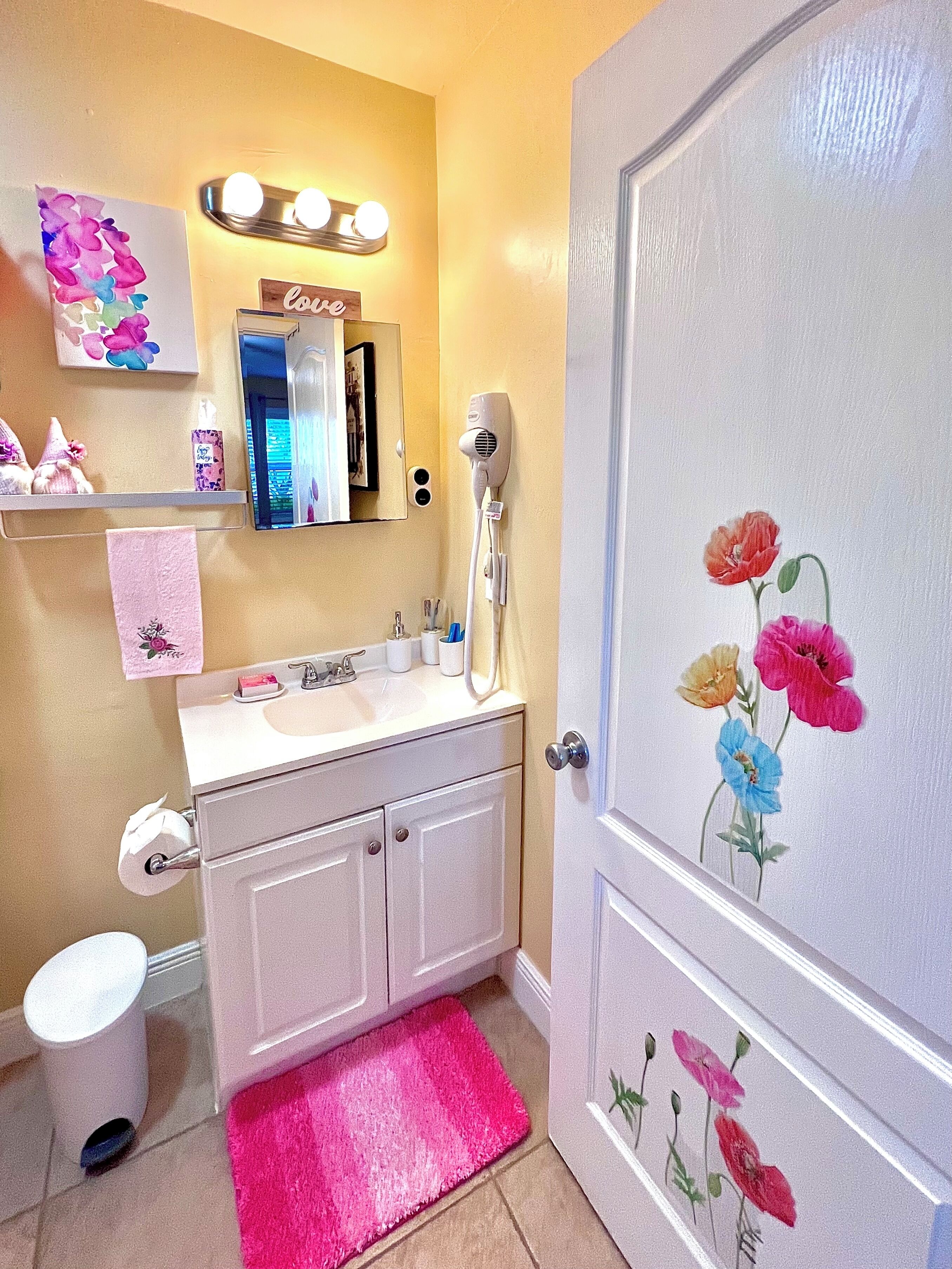 Une salle de bain équipée d’un lavabo, d’un miroir, d’un porte-serviettes et d’une porte ornée de motifs floraux.
