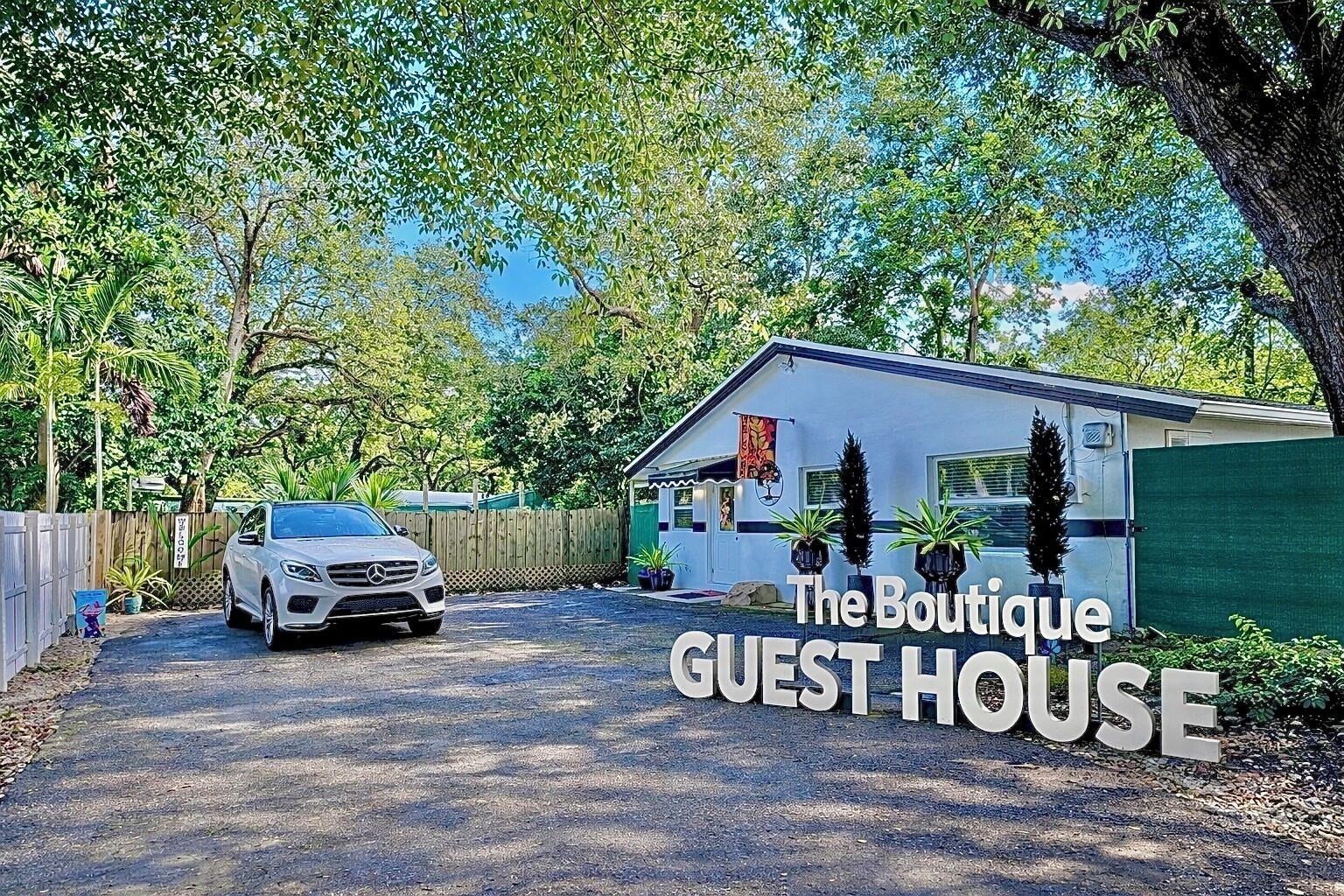 A white car parked in front of a building labeled 'The Boutique GUEST HOUSE' with a paved driveway and surrounding greenery.