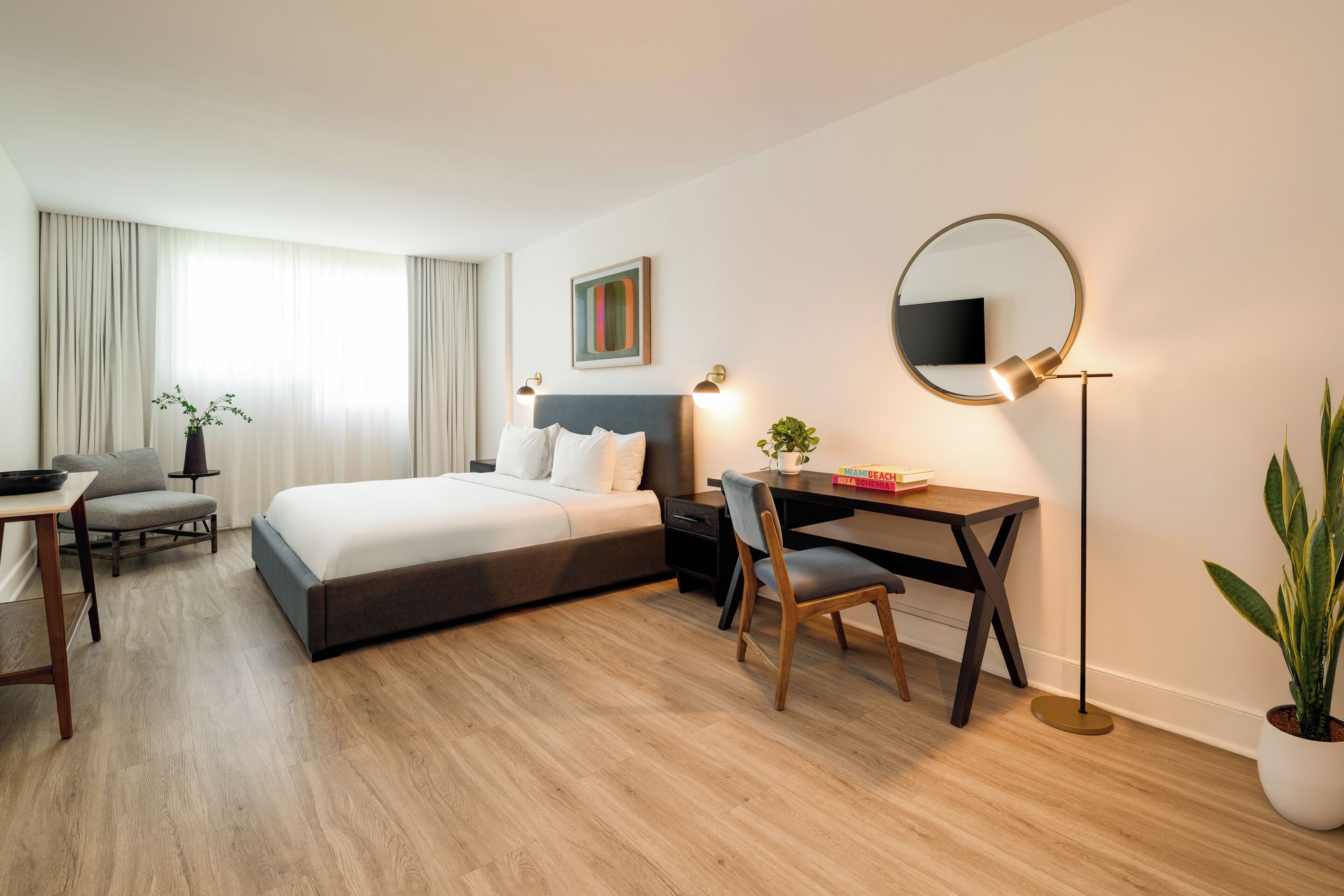 Une chambre d’hôtel moderne équipée d’un lit, d’un bureau, d’une chaise et d’un miroir rond.