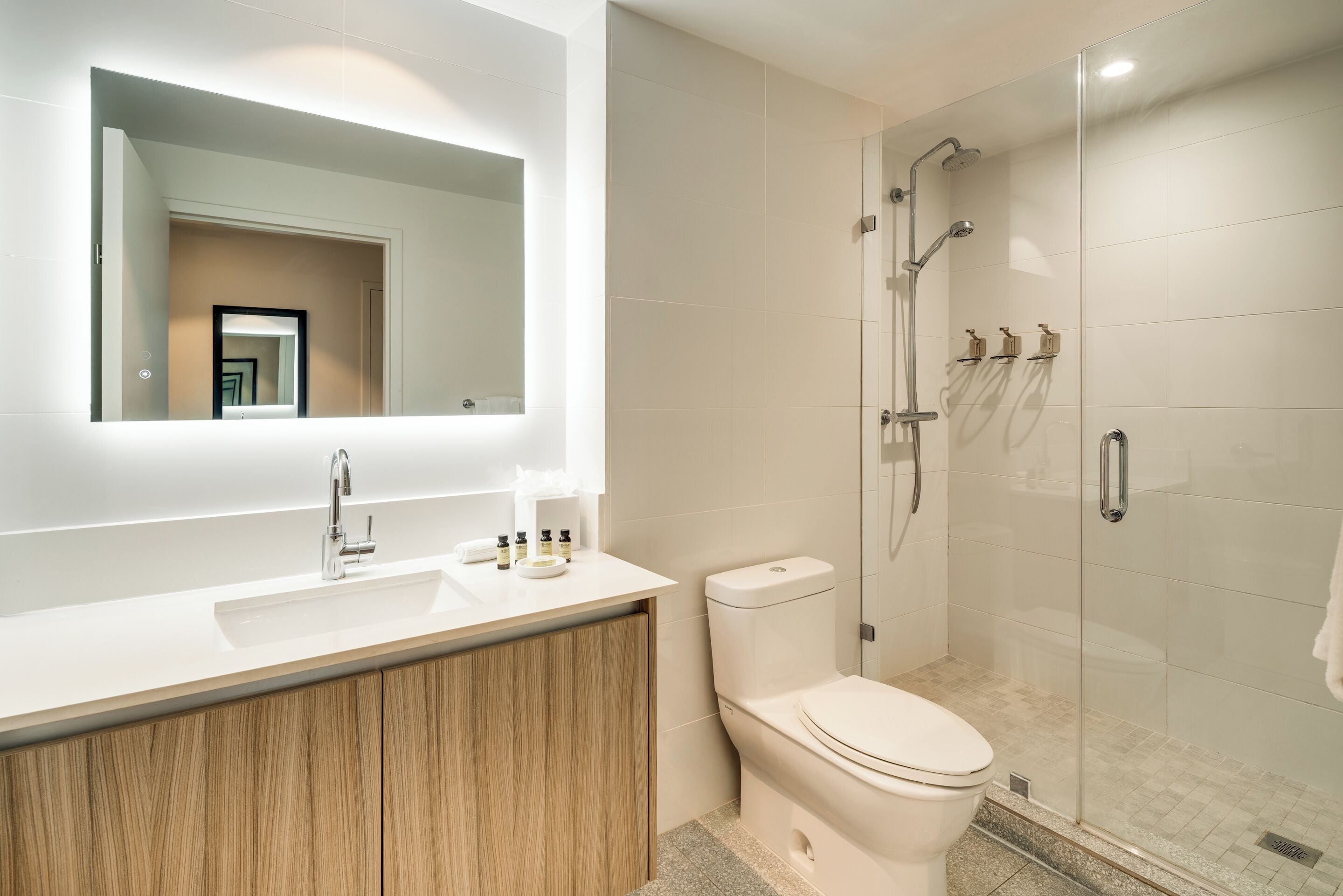 A modern bathroom with a white sink, wooden vanity, a toilet, and a glass-enclosed shower area.