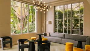 A modern interior with large windows, a grey sofa, black and yellow chairs, and a unique light fixture. - Kenmore Village Hotel, South Beach (Miami Beach)