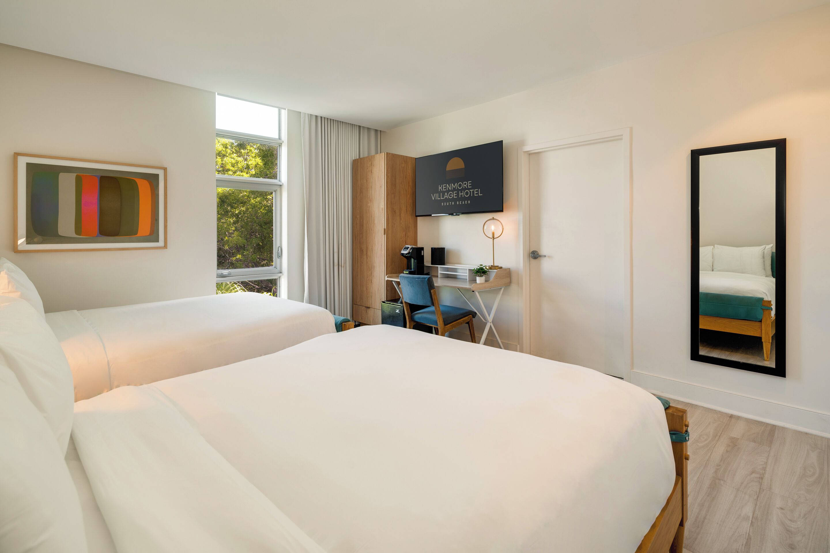 A hotel room with two beds, a desk, a chair, a coffee machine, a TV, and a large window.