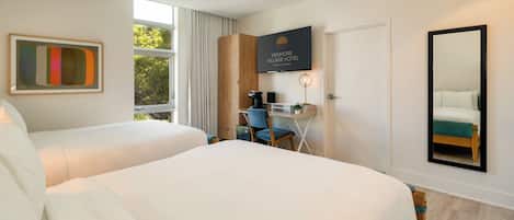 A hotel room with two beds, a desk, a chair, a coffee machine, a TV, and a large window.