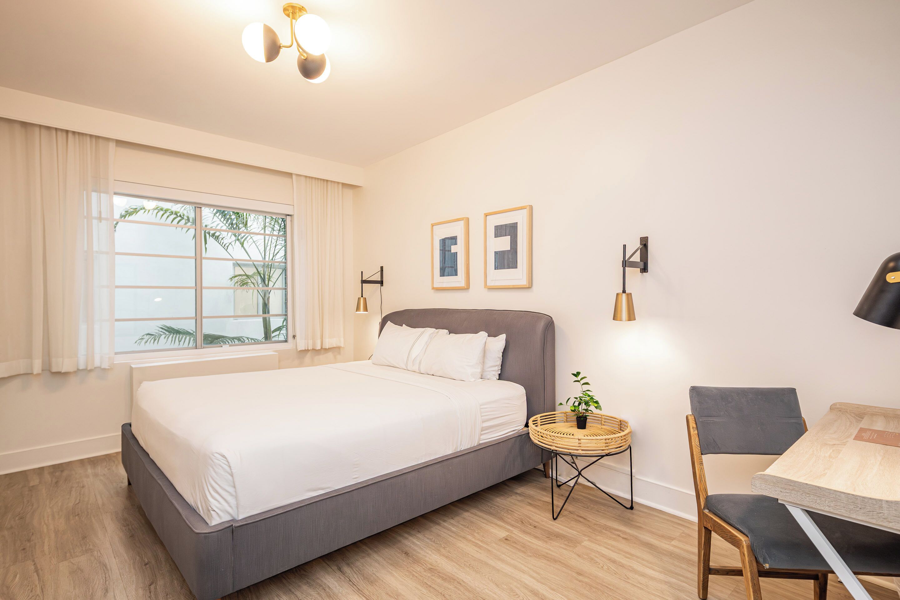 Quarto moderno com uma cama grande, uma mesinha redonda com uma planta, uma cadeira e duas imagens emolduradas na parede.