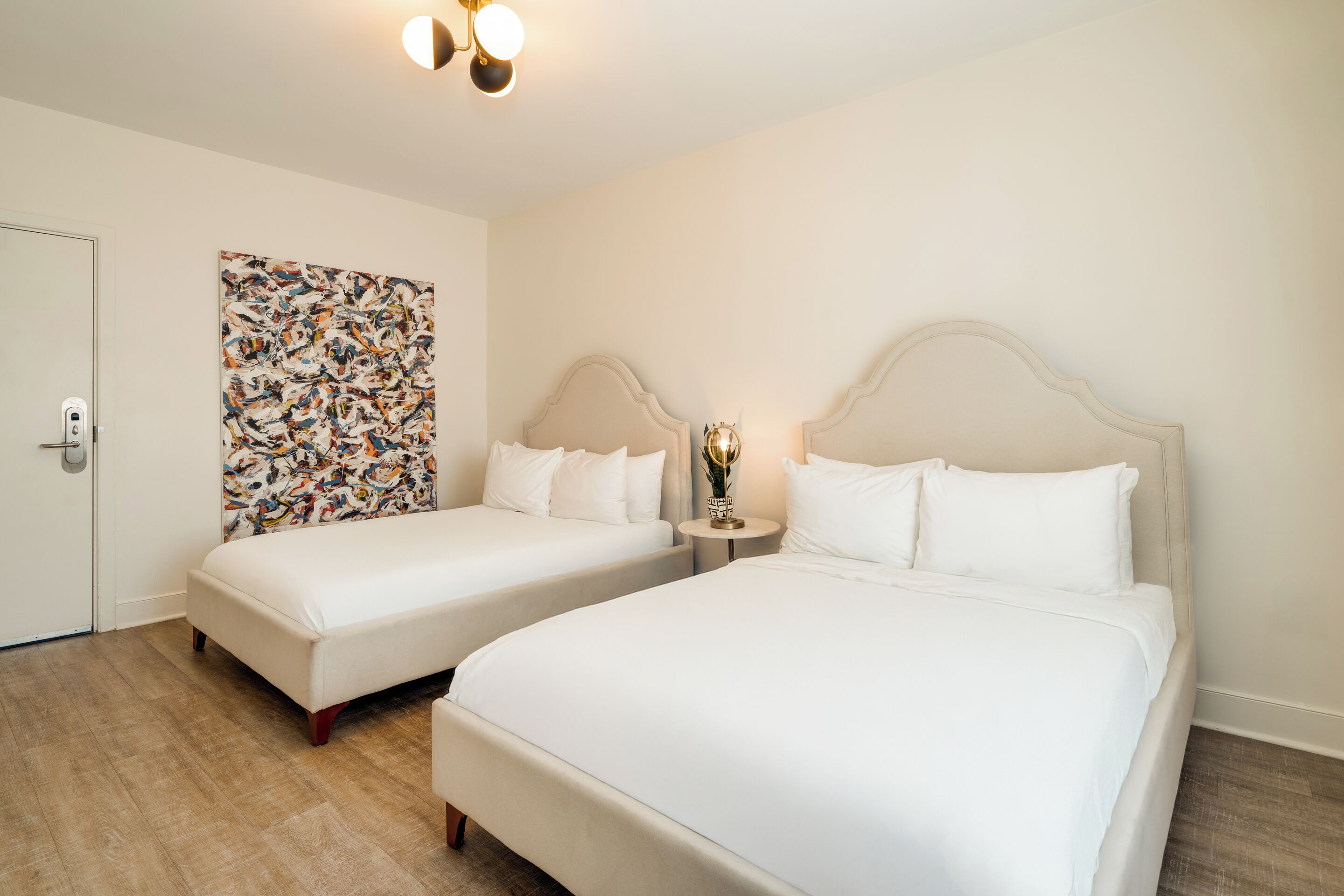 A hotel room with two beds, a large abstract painting on the wall, and a small table with a lamp.