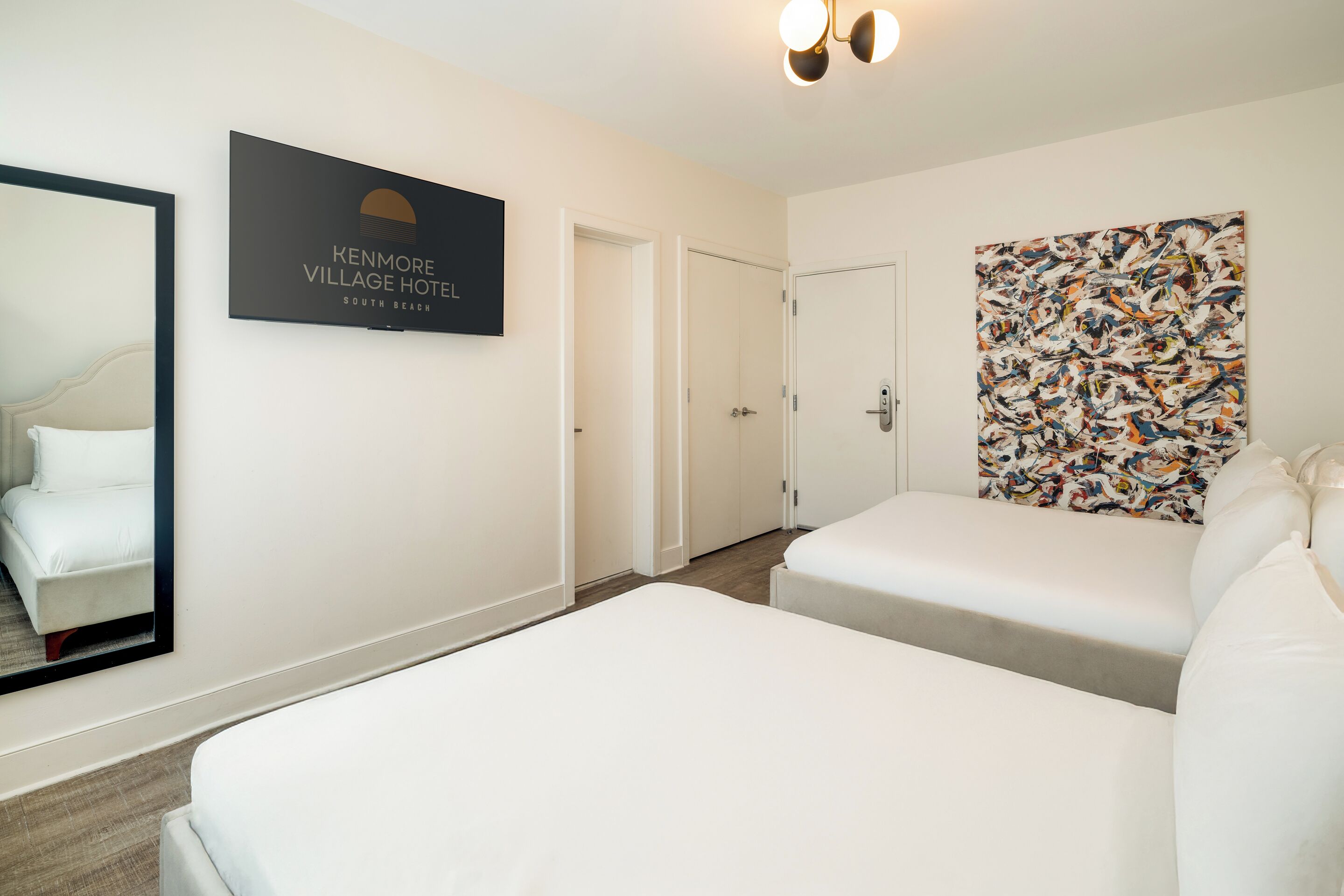 A hotel room with two beds, a large mirror, a framed sign, and a colorful abstract painting.