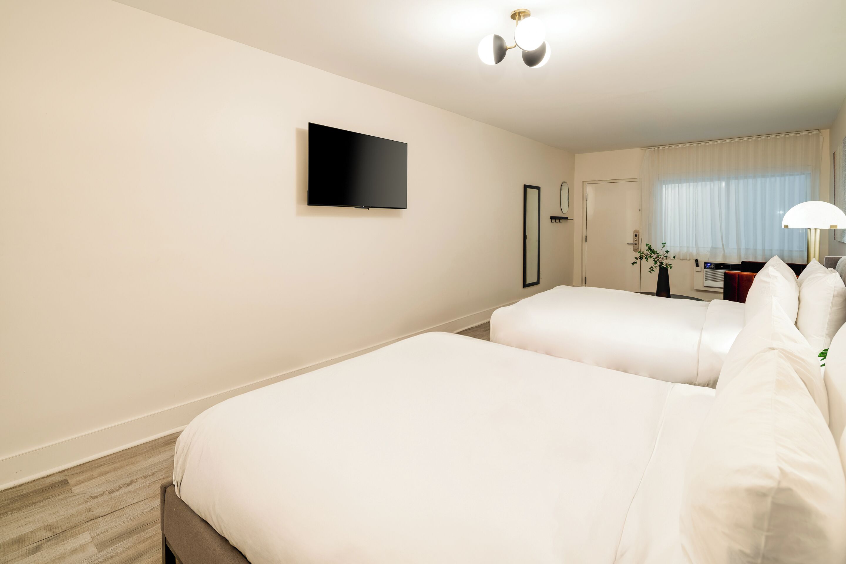 Une chambre d’hôtel avec deux lits, un téléviseur à écran plat, une table de chevet avec une lampe et une fenêtre avec des rideaux.