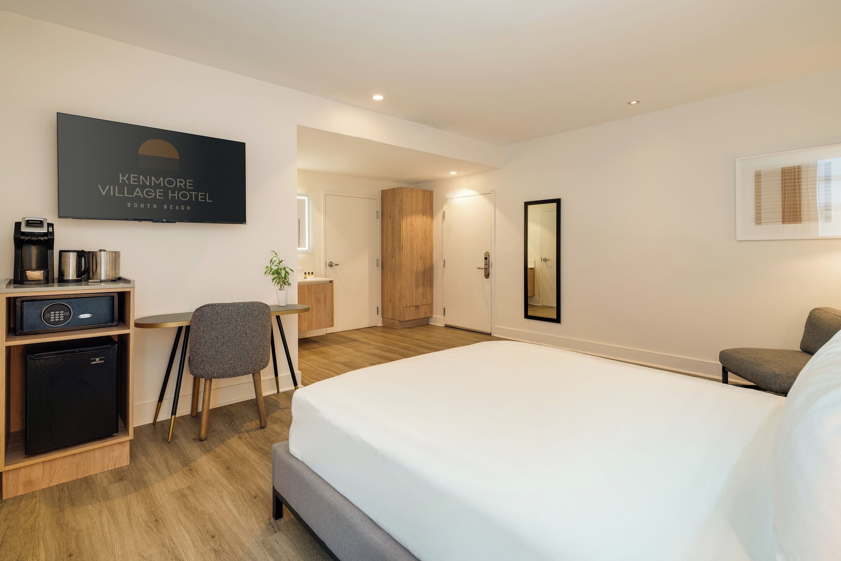 A hotel room with a bed, desk, chair, and a television displaying the hotel name.
