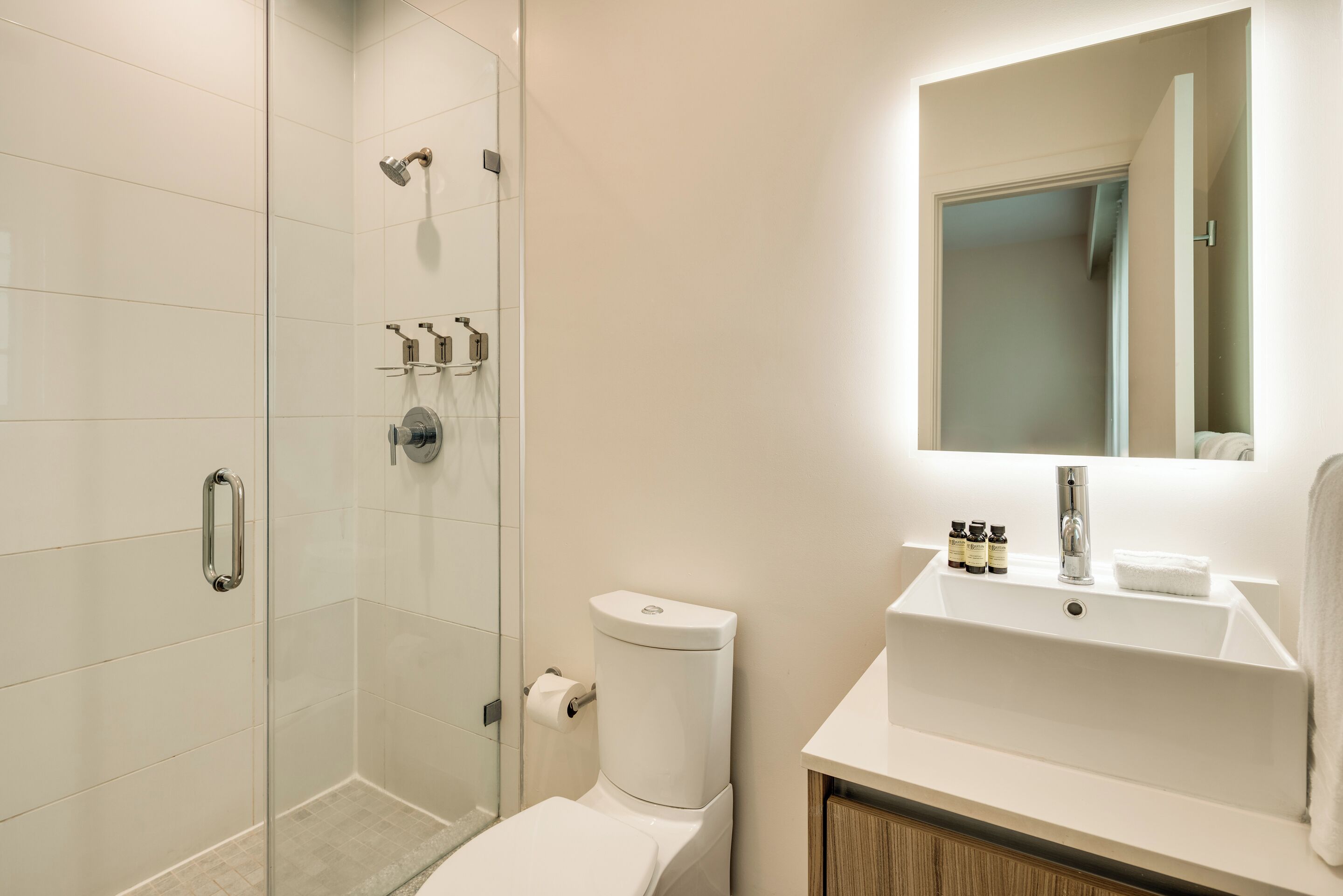 Une salle de bain moderne avec une douche à parois de verre, des toilettes et un lavabo surmonté d’un miroir.