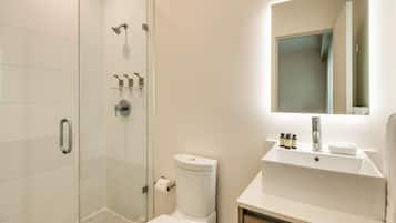 Une salle de bain moderne avec une douche à parois de verre, des toilettes et un lavabo surmonté d’un miroir.