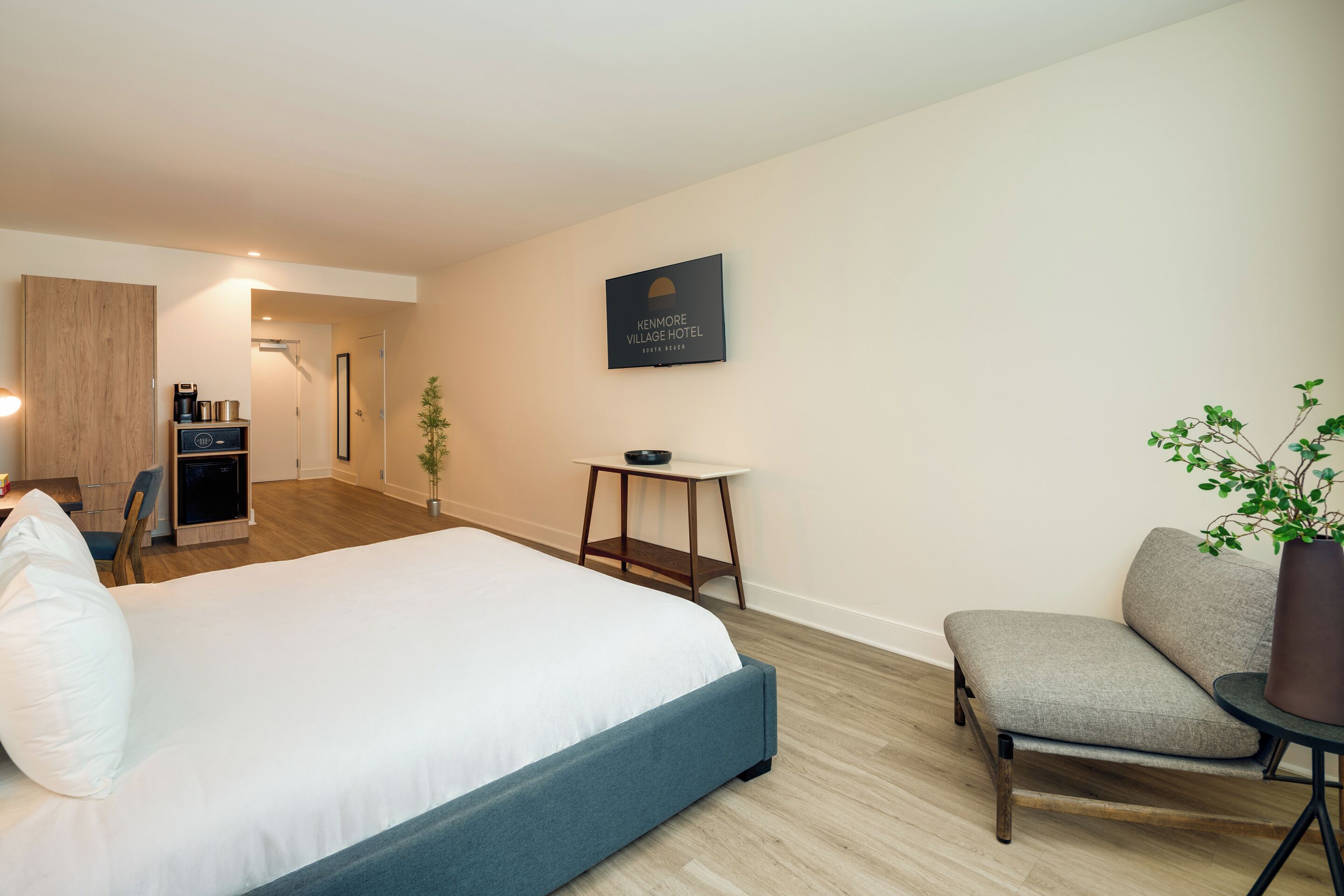 Una habitación de hotel moderna con una cama grande, un rincón de descanso con una silla y una mesa, una mesita auxiliar pequeña y un letrero en la pared.