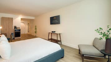 Una habitación de hotel moderna con una cama grande, un rincón de descanso con una silla y una mesa, una mesita auxiliar pequeña y un letrero en la pared.