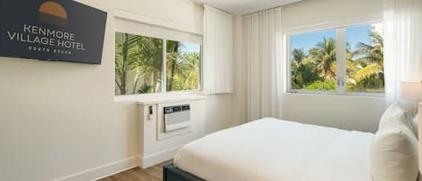 Una habitación de hotel con una cama grande, dos ventanas con cortinas, un aire acondicionado montado en la pared y un letrero que dice Kenmore Village Hotel.