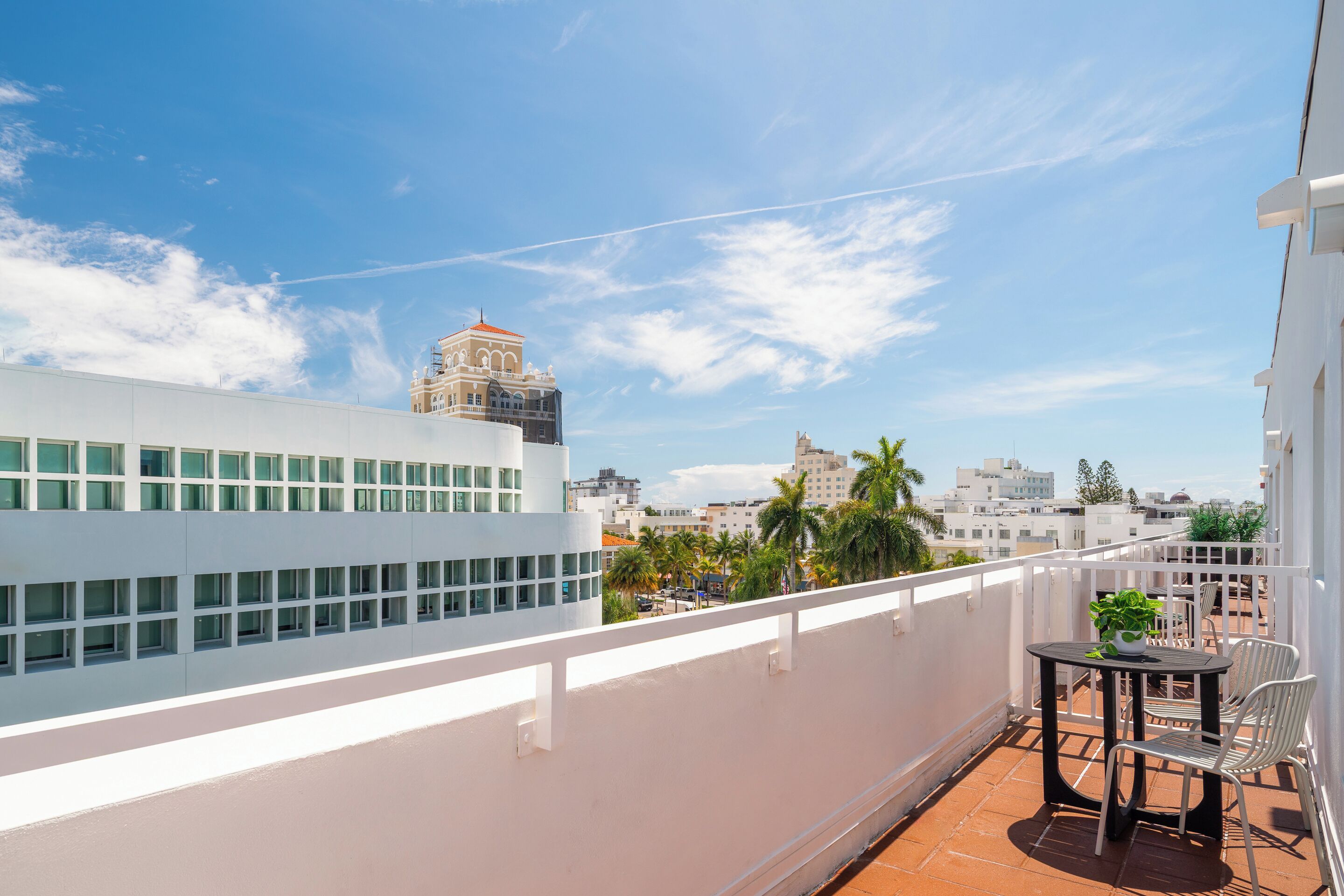 Terraza en la azotea con una mesa y sillas, con vistas a un paisaje urbano que incluye edificios modernos y palmeras.
