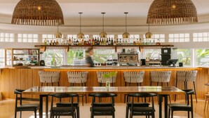 A bar area with a long wooden counter, wicker pendant lights, and a variety of bottles. - Kenmore Village Hotel, South Beach (Miami Beach)