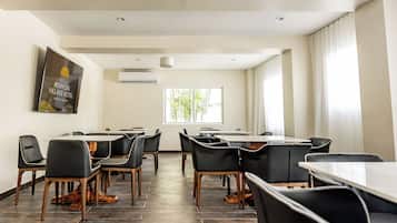 Une salle de conférence équipée d’une grande table et de nombreuses chaises, d’un climatiseur et d’une fenêtre avec des rideaux.