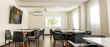 A conference room with a large table and multiple chairs, an air conditioning unit, and a window with curtains.