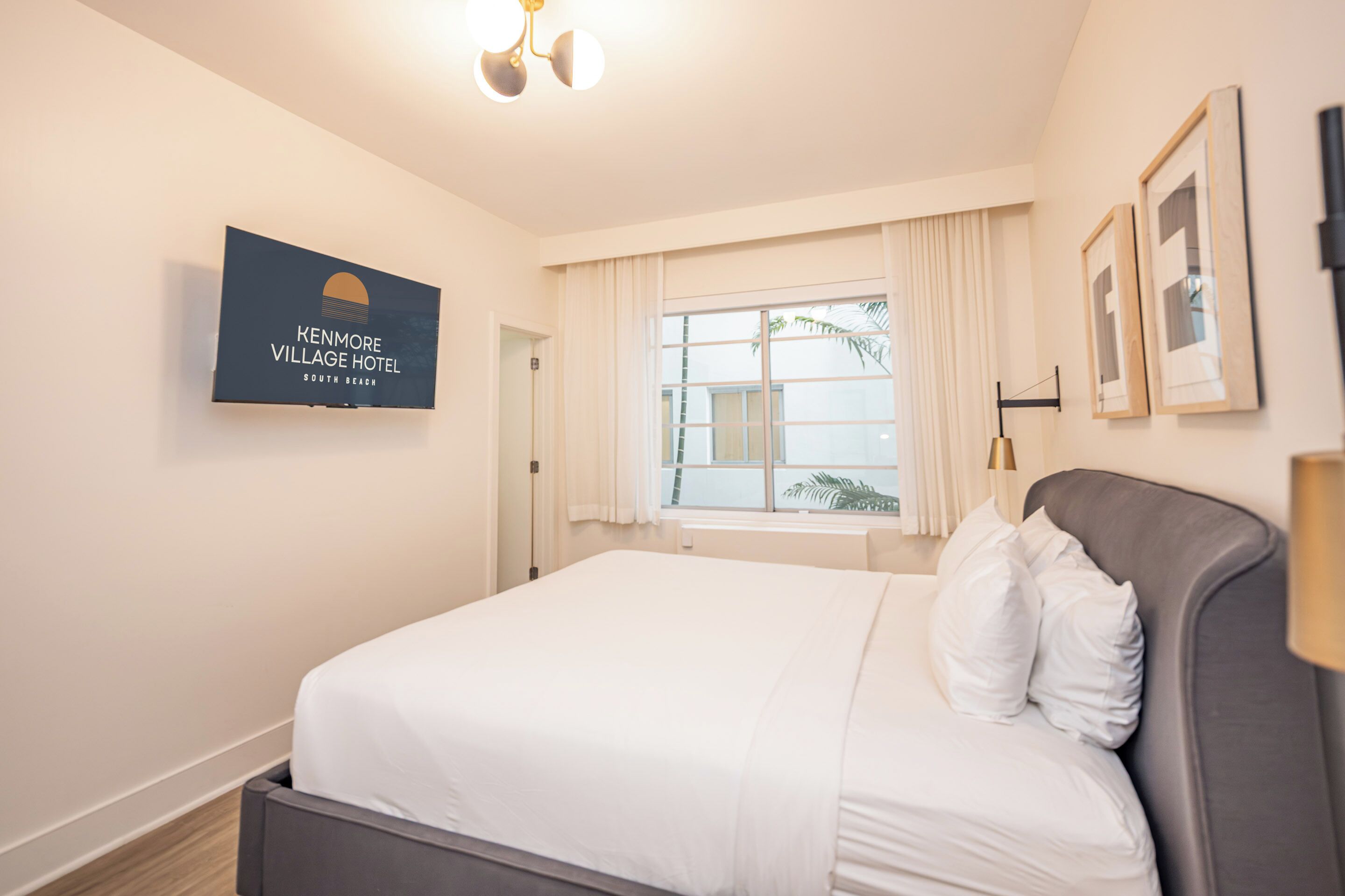 Ein Hotelzimmer mit Bett, einem Fenster mit Vorhängen, einem Wandzeichen und einem gerahmten Bild.