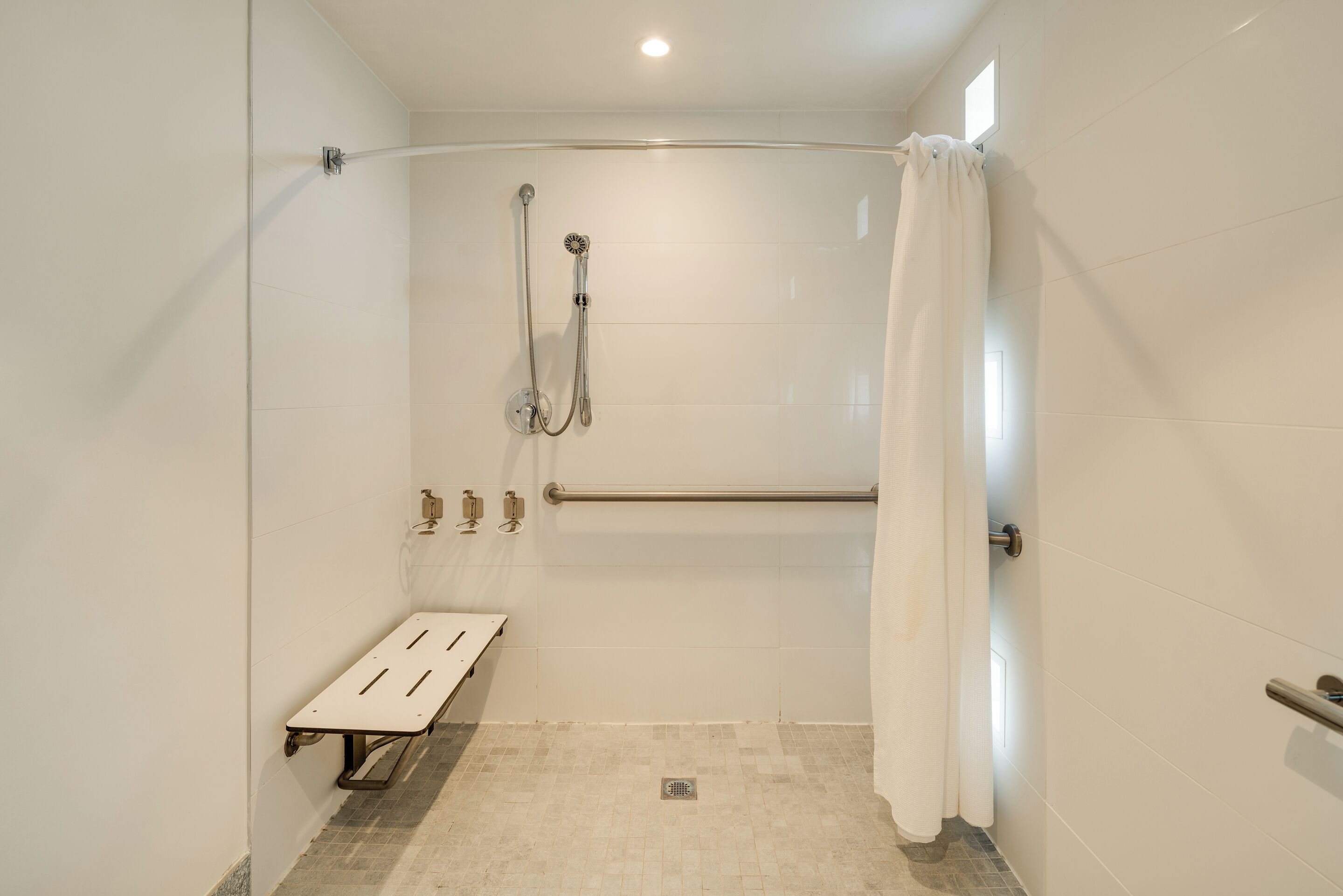 A shower area with a bench, grab bars, and a showerhead.