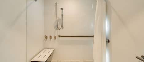 A shower area with a bench, grab bars, and a showerhead.